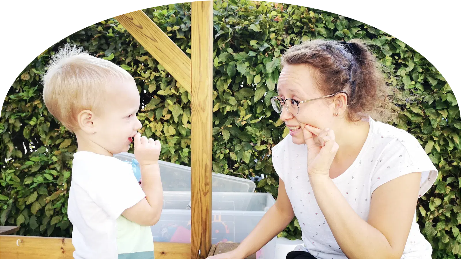 Mutter und Kind sitzen sich im Garten gegenüber und kommunizieren mit Gebärden
