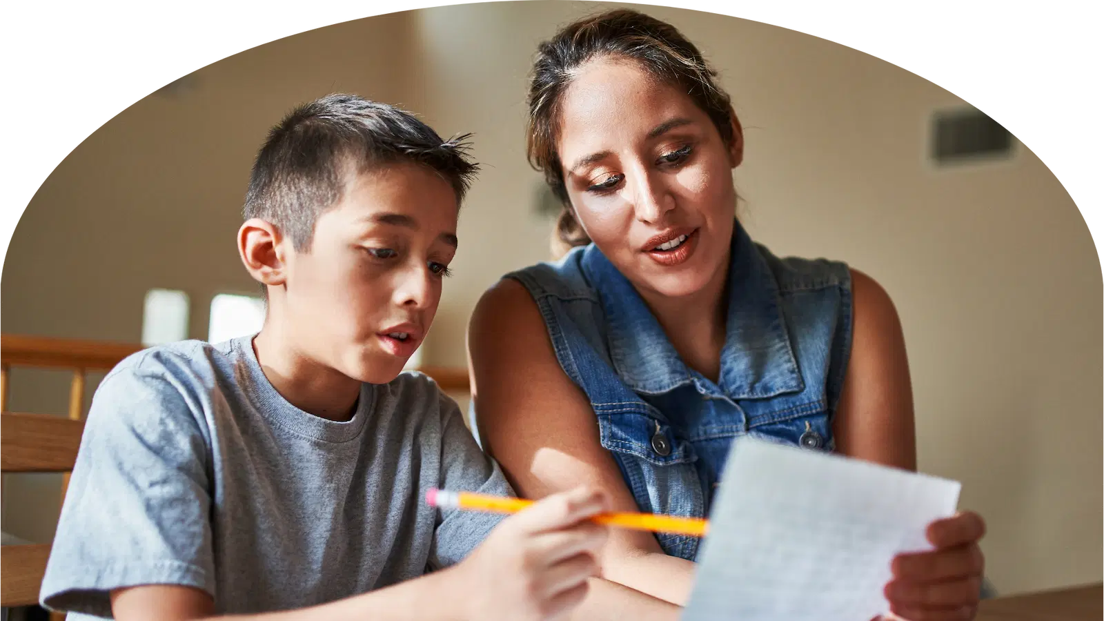 Mutter und Sohn sitzen nebeneinander am Tisch und schauen gemeinsam auf ein Blatt Papier, der Sohn hält einen Bleistift